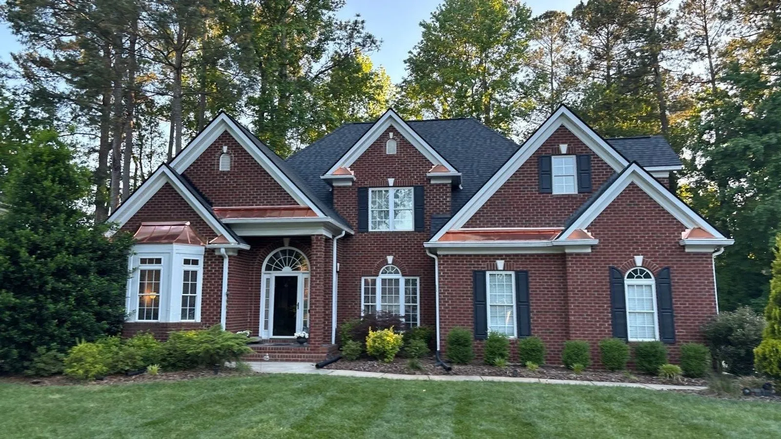 A finished brick Carolina home with a dark shingle roof and custom copper bay-window roofs by Old North Roofing